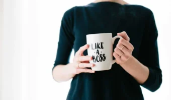 Una persona con una camiseta negra sostiene una taza blanca con la frase "LIKE A BOSS" impresa, lo que refleja una fuerte marca personal.