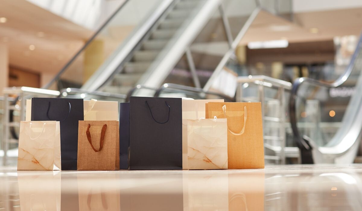 Bolsas de compras creativas descansan en el suelo del centro comercial con escaleras mecánicas que suben en el fondo.