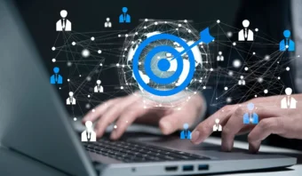 Manos escribiendo en un teclado de computadora portátil con un objetivo digital, o “el target”, y una red de íconos de usuarios conectados superpuestos, que simbolizan el marketing digital o la creación de redes específicas.