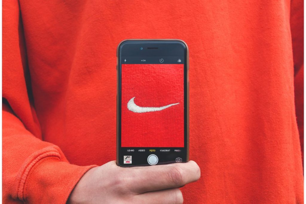 Persona sosteniendo un teléfono 
 móvil para tomar una fotografia a Nike como Marca de Culto