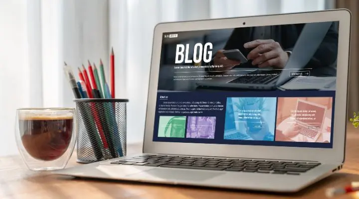 Una laptop sobre un escritorio muestra la página de un blog enfocado en el SEO. Junto a ella hay un vaso de café y un soporte metálico con lápices de colores.
