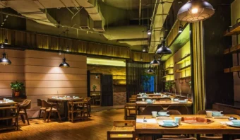 Un interior de restaurante moderno con mesas y sillas de madera, platos y tazas, iluminación cálida y plantas decorativas, que ofrece un ambiente acogedor a diferencia de los típicos restaurantes fantasmas.