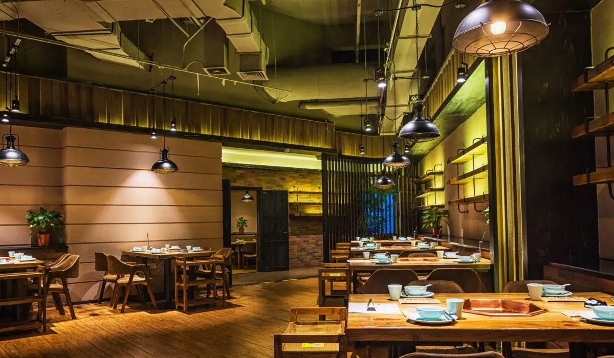 Un interior de restaurante moderno con mesas y sillas de madera, platos y tazas, iluminación cálida y plantas decorativas, que ofrece un ambiente acogedor a diferencia de los típicos restaurantes fantasmas.