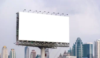 Un gran cartel blanco vacío se encuentra en un poste de metal sobre los edificios de la ciudad contra un cielo nublado, listo para mostrar anuncios creativos para captar la atención de los transeúntes.