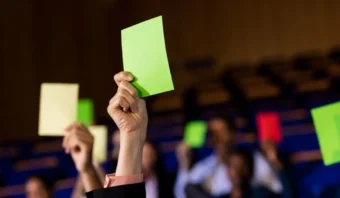 Varias personas en una audiencia sostienen tarjetas verdes y amarillas, posiblemente participando en un proceso de votación o decisión grupal durante un evento de no presentación.