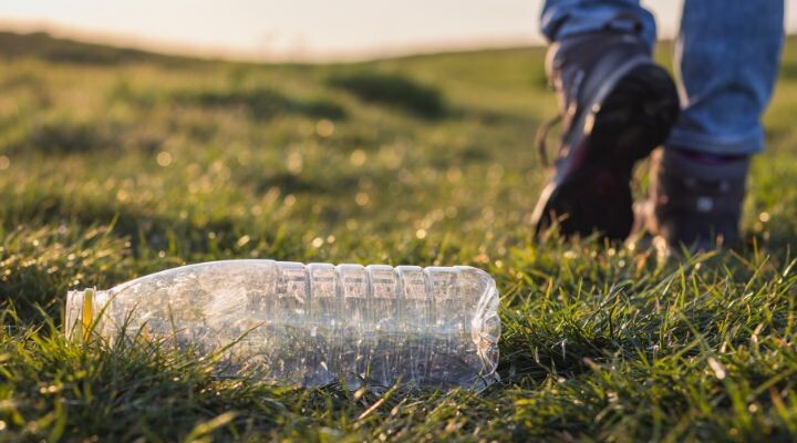 Un acto irresponsable ocurre cuando una botella de plástico yace en el pasto, mientras una persona se aleja caminando en el fondo, irresponsables somos