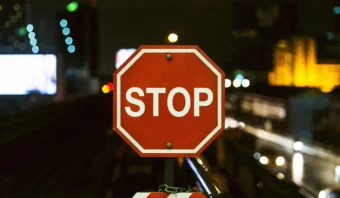 Una señal de pare octogonal de color rojo se muestra de noche con luces de la ciudad y edificios borrosos en el fondo, evocando sutilmente la idea de los pecados capitales de Internet y recordándonos que debemos hacer una pausa antes de cruzar los límites digitales.