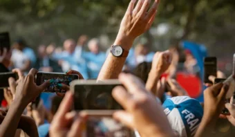 La gente en una multitud levanta los brazos y toma fotos o videos con sus teléfonos; un brazo, con un reloj, sobresale. Momentos como estos suelen viralizarse, poniendo de relieve el papel de las redes sociales en el deporte.