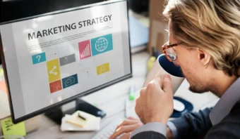 Una estrategia de marketing digital bebe de una taza mientras mira una pantalla de computadora que muestra un plan de estrategia de marketing con gráficos y cuadros.