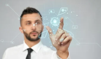 Un hombre con camisa blanca y corbata interactúa con una interfaz digital transparente, tocando íconos virtuales mientras explora qué nos depara el 2025 en el cambiante mundo de la tecnología.