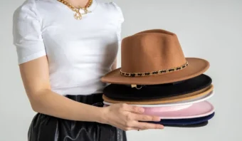 Una persona con una camisa blanca sostiene una pila de sombreros de varios colores, evocando la estrategia de los 6 sombreros, con un sombrero marrón que presenta una banda estampada en la parte superior.