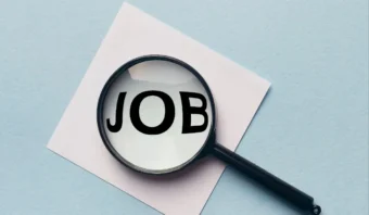 Una lupa colocada sobre un papel blanco se enfoca en la palabra “JOB” escrita en letras negras en negrita, que simboliza la búsqueda para encontrar trabajo.