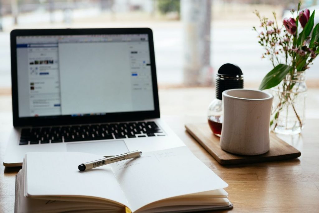 Una de trabajo con un cuaderno, café, flores y una computadora mostrando anuncios creativos