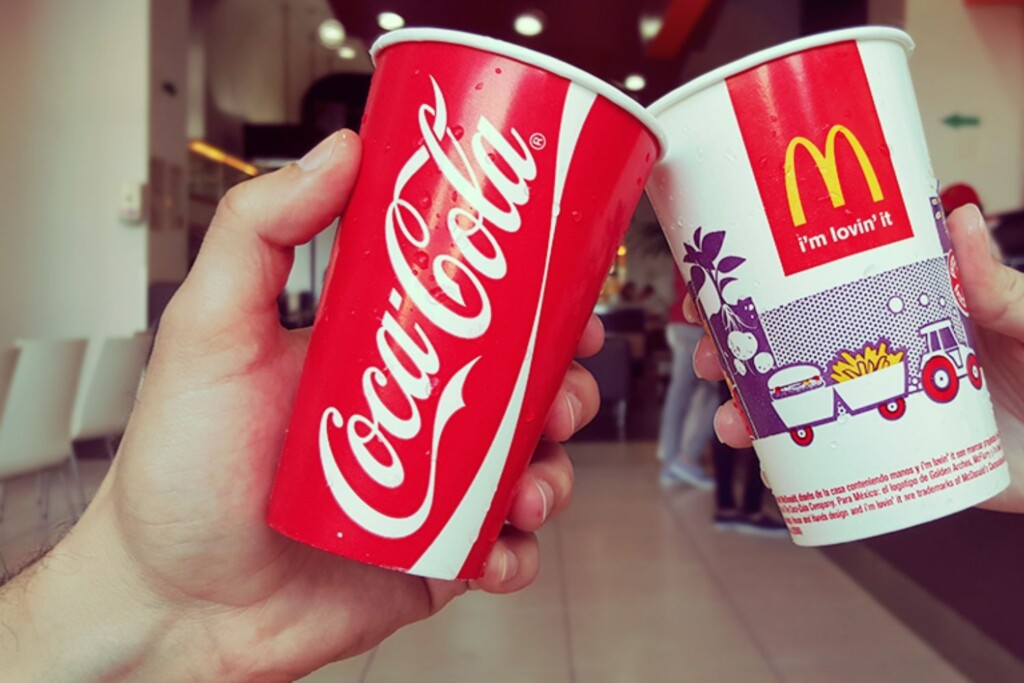 Dos personas sosteniendo una copa de mcdonald's y una copa de coca cola.