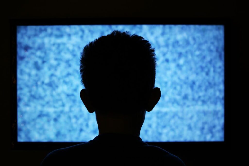 La silueta de un niño mirando televisión en la oscuridad, cautivado por los buenos comerciales.