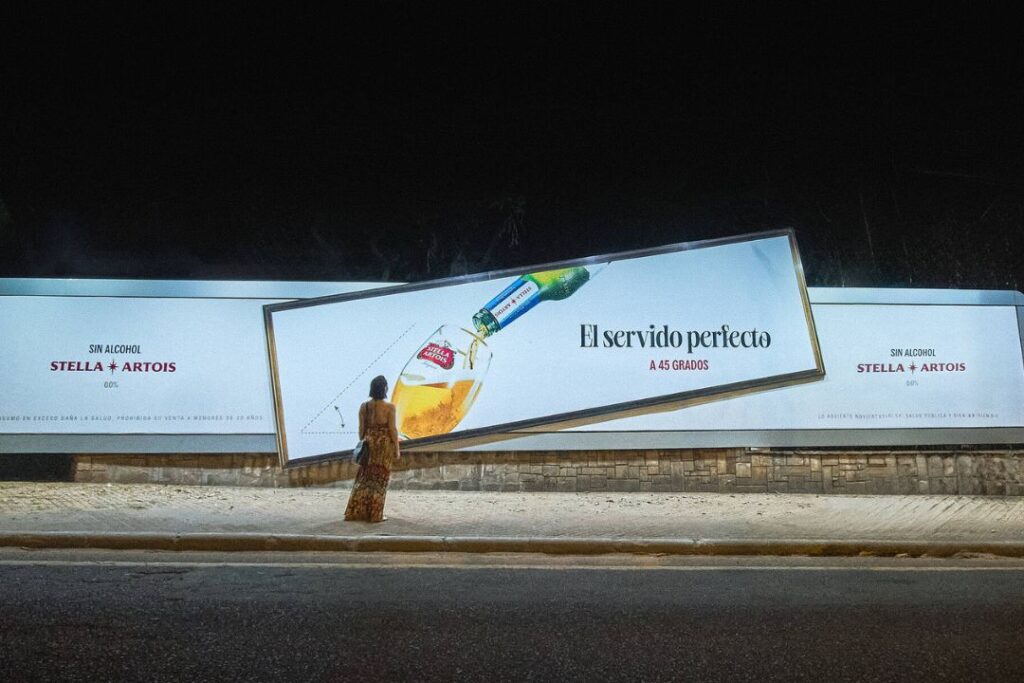 Un hombre está de pie junto a un cartel que anuncia una cerveza Stella Artois.