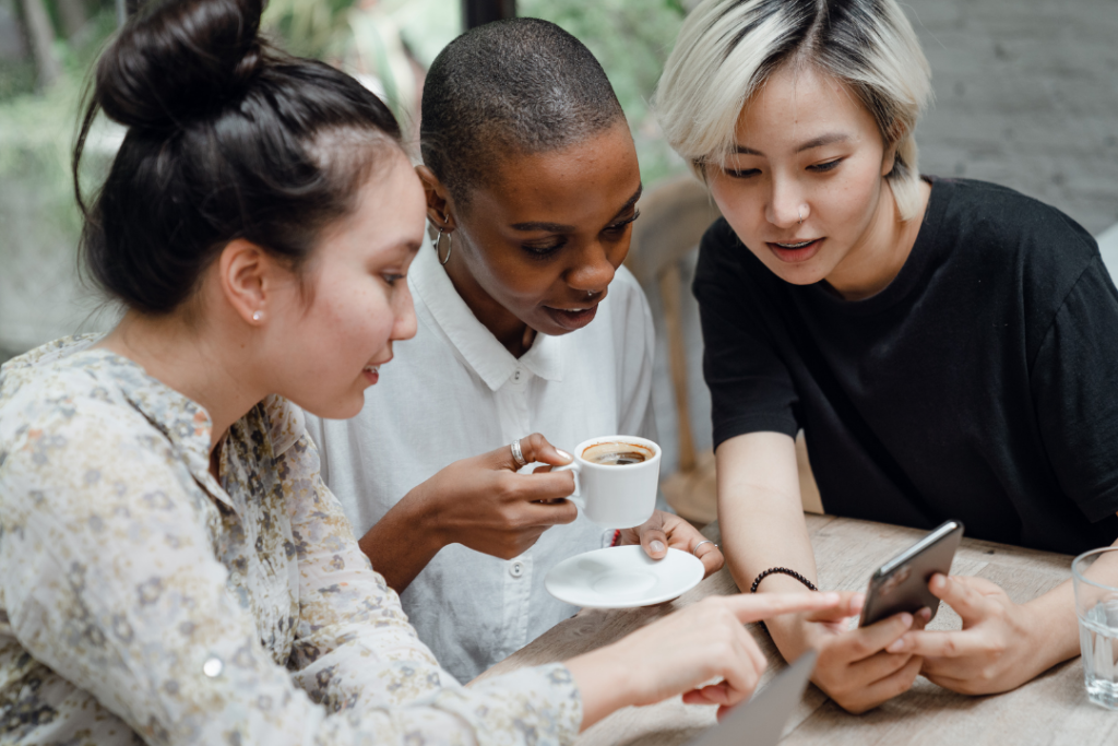 Tres mujeres sentadas alrededor de una mesa mirando un teléfono celular mirando la tendencia en México.