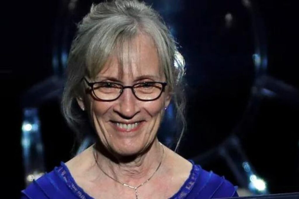 Una mujer sonriente y con gafas sostiene un premio de economía en el cual destaca la brecha de género.