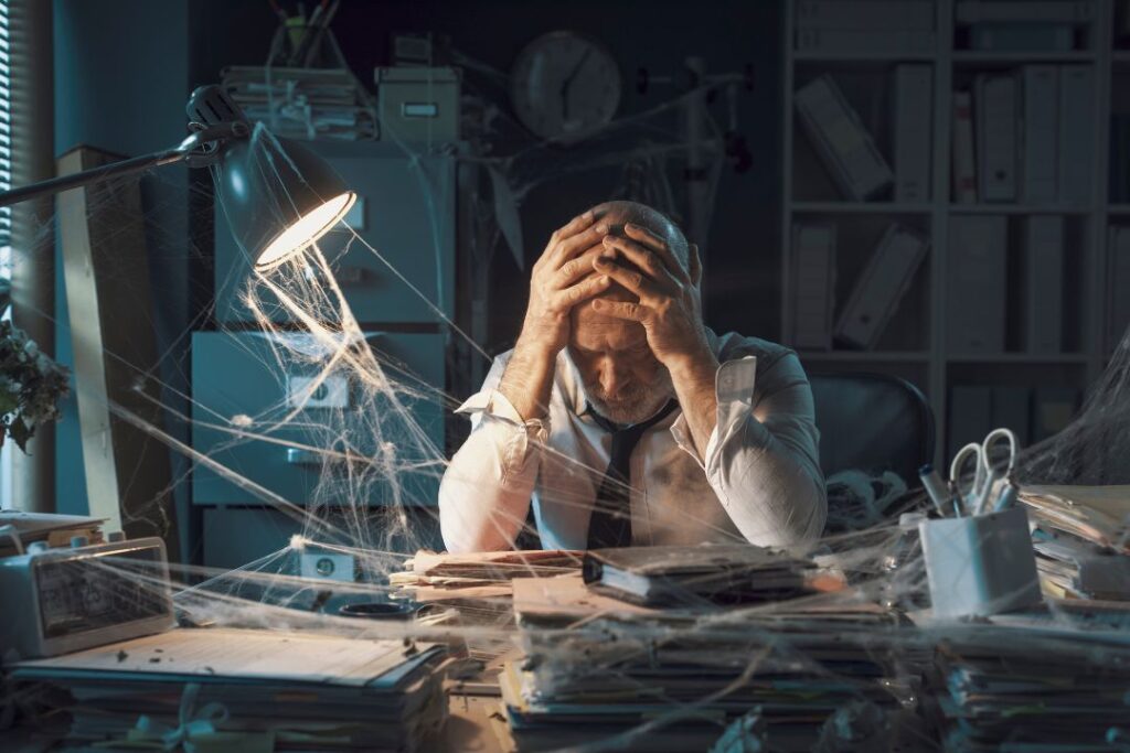 Un hombre que atraviesa una crisis en su escritorio con telas de araña en la cabeza.