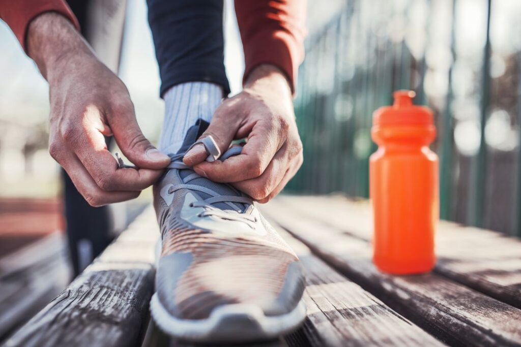 Un hombre atándose los zapatos en un banco preparado para practicar deportes.