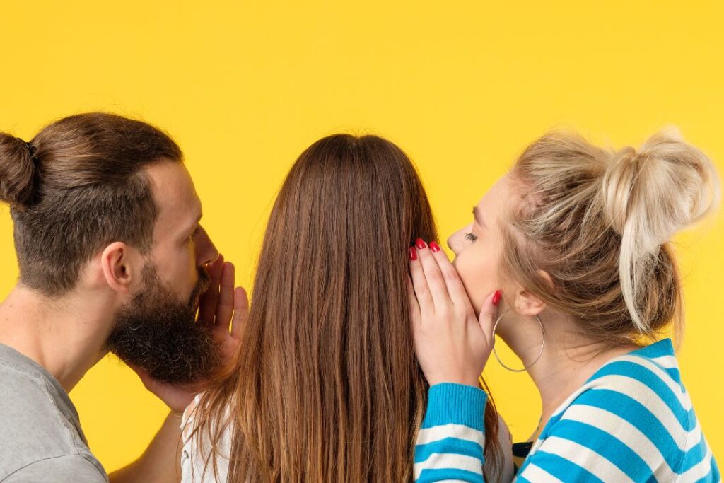 Tres jóvenes susurrando entre sí sobre un fondo amarillo, representando la persuasión.