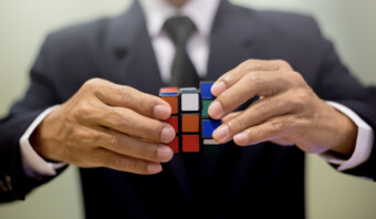 Un hombre de negocios que porta un maletín y sostiene un cubo de Rubik para hacer un brief.