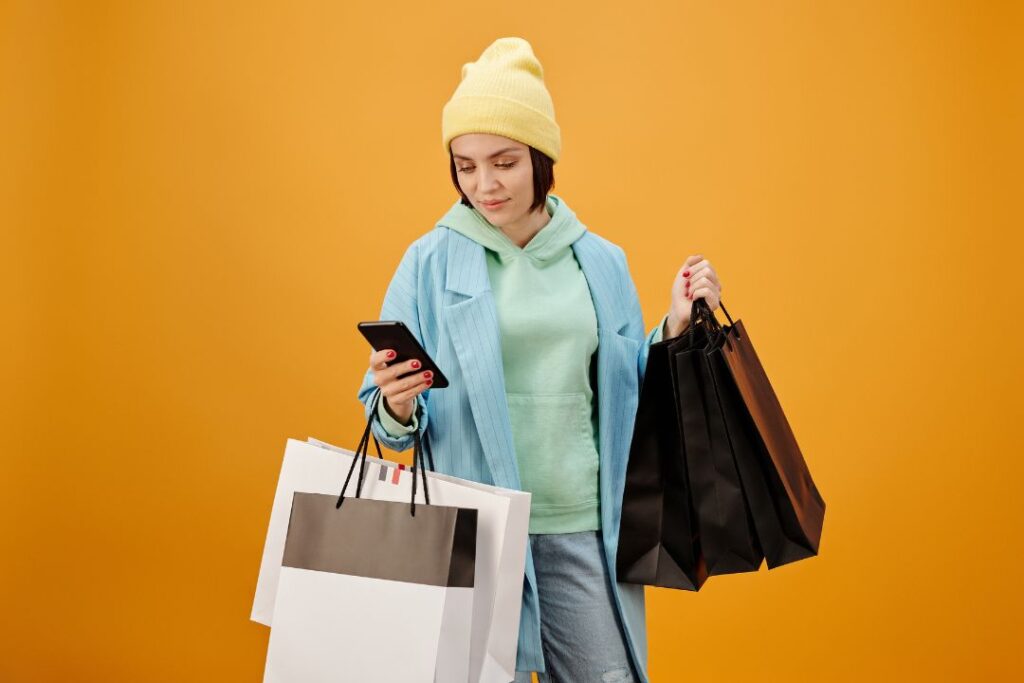 Una mujer con bolsas de compras y un celular sobre fondo naranja durante el Buen Fin 2023.