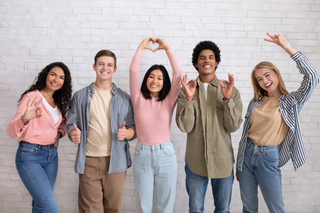 Descripción: Un grupo de jóvenes haciendo una señal de corazón frente a un muro de ladrillos.