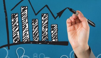 Una mano dibujando un gráfico de barras sobre un fondo azul para visualizar Tendencias de relaciones públicas.