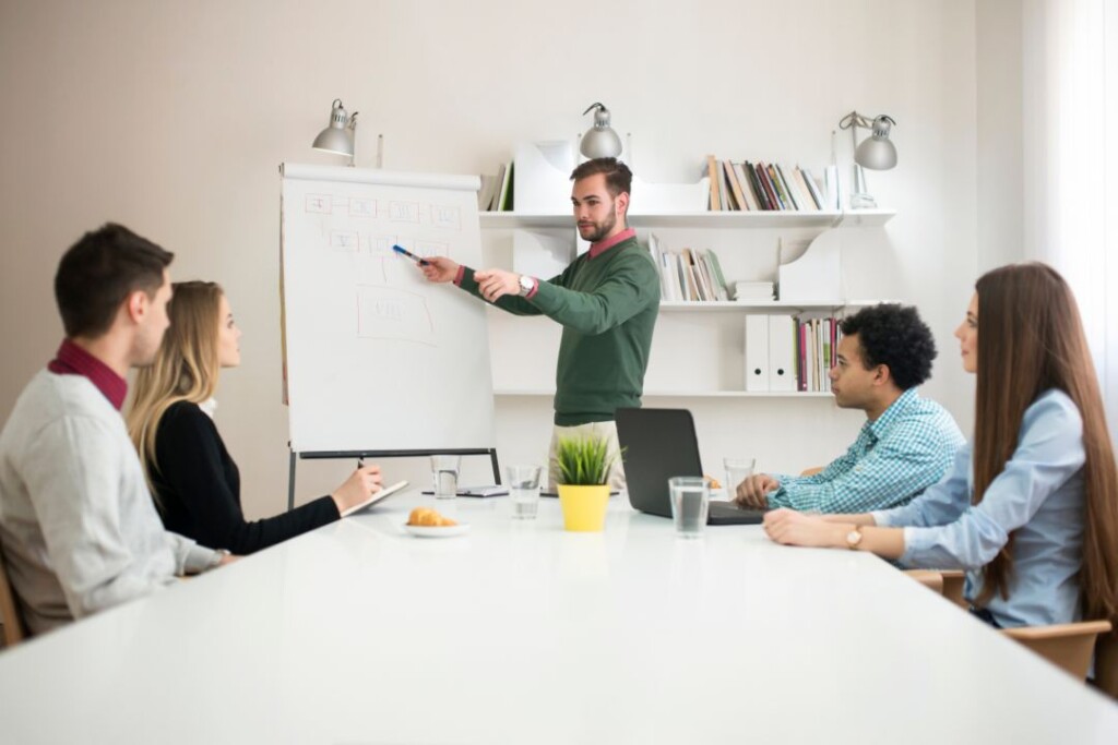 Un grupo de personas discutiendo tendencias de relaciones públicas mientras están sentadas alrededor de una pizarra en una sala de reuniones.