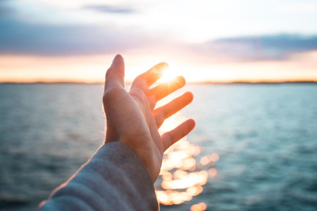 La mano de una persona extendiéndose hacia el sol, llena de esperanza y deseos.