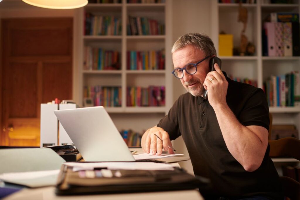 Un hombre practicando teletrabajo, sentado en un escritorio con una computadora portátil y un teléfono celular.