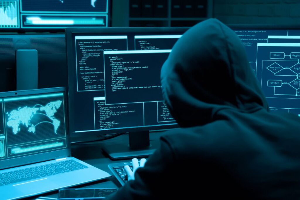 Un hombre con sudadera con capucha sentado frente a una computadora, posiblemente trabajando en ransomware.