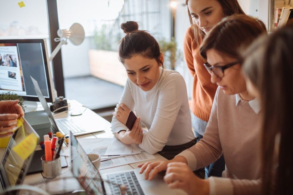 Un grupo de mujeres trabajando en una computadora portátil en una oficina usando la guía gratuita como referencia.