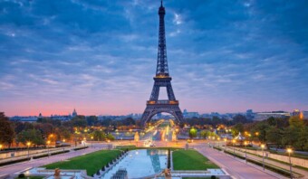 Vista temprano en la mañana de la Torre Eiffel en París 24, con farolas iluminadas y un cielo azul claro, con vistas a los jardines del Trocadero y las fuentes de agua.