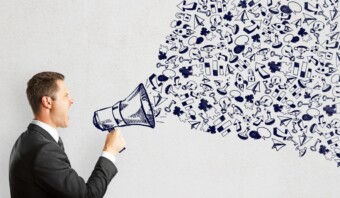 Una persona con traje sostiene un megáfono con varios garabatos y símbolos azules, que representan la voz dinámica de la marca, sobre un fondo blanco.