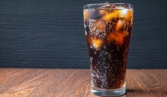 Un vaso de Dr. Pepper oscuro y carbonatado con cubitos de hielo se asienta sobre una superficie de madera sobre un fondo oscuro.