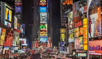 Una vista nocturna de Times Square con vallas publicitarias brillantemente iluminadas, anuncios digitales vibrantes y calles abarrotadas de gente y vehículos crea un centro de marketing dinámico que recuerda a las bulliciosas redes sociales.