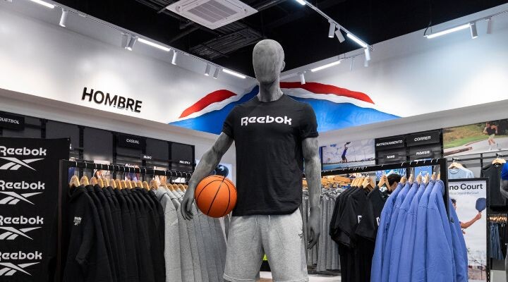 Un maniquí con camiseta y pantalones cortos Reebok sostiene una pelota de baloncesto en la sección "Hombre" de la tienda de ropa deportiva de Mundo E.