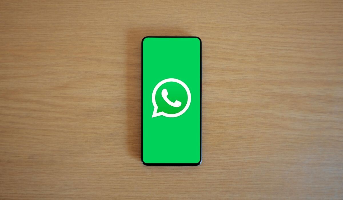 Teléfono inteligente sobre una superficie de madera que muestra el logotipo de WhatsApp Business en su pantalla.