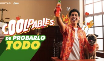 Una persona con una camiseta naranja sostiene una botella de gaseosa, sonriendo, junto a un carlino sobre una mesa. El texto dice "Coolpables de Probarlo Todo". Al fondo se ve una decoración luminosa y una ventana.