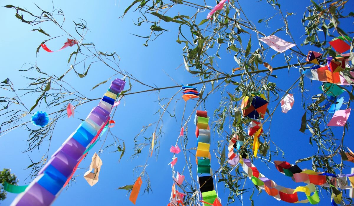 Decoraciones de papel coloridas cuelgan de las ramas de los árboles, creando una escena vibrante que recuerda el espíritu animado del Festival ElDorado, todo ello ambientado contra un cielo azul claro.
