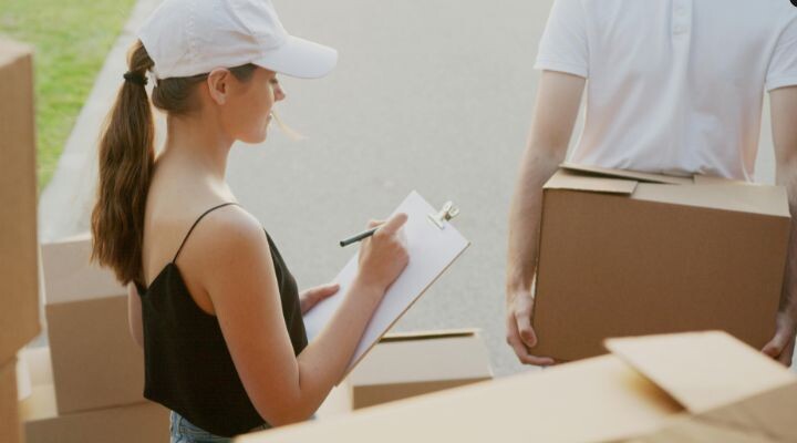 Una mujer con un portapapeles marca cajas mientras una persona sostiene una caja. fuga de talento 