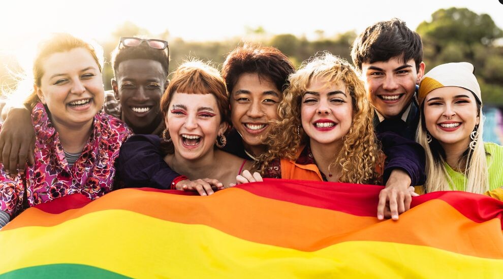 Un grupo diverso de personas sonriendo y sosteniendo una bandera del arcoíris, que representa el orgullo LGBTQ+. marketing inclusivo