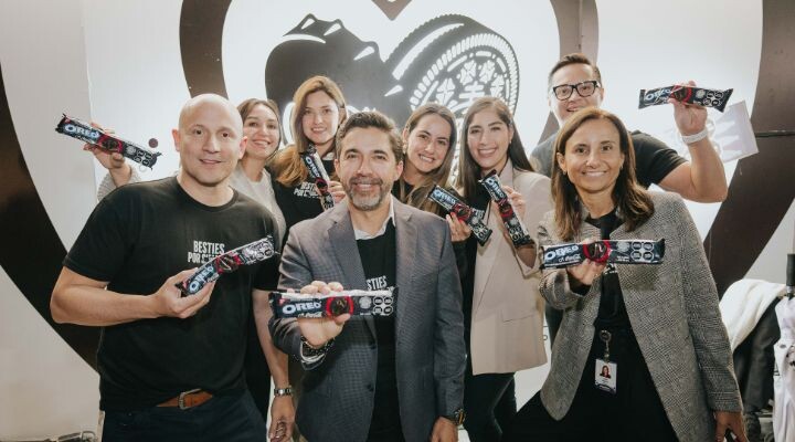 Un grupo de personas sonriendo y sosteniendo paquetes de Oreo frente a un gran fondo con el logo de Oreo, como si estuvieran celebrando un momento Oreo y Coca-Cola.