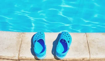 Un par de Crocs azules se encuentran en el borde de una piscina; su tono vibrante refleja el agua azul clara.