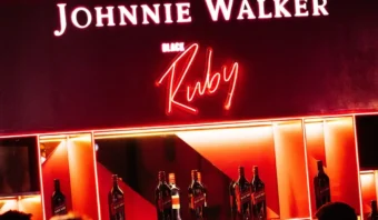 Estante de bar con letrero y botellas de Johnnie Walker Black Ruby iluminados, que ofrece un elegante guiño a la innovación, muy similar a la combinación perfecta de inteligencia artificial y moda en el mundo de la moda actual.