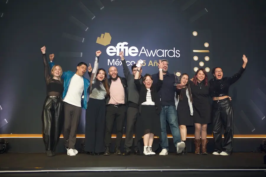 Un grupo de personas se encuentra en el escenario con los brazos en alto en celebración en el evento de los Premios Effie, representando orgullosamente a Isla República.