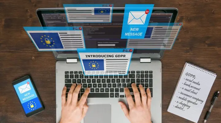 Manos escribiendo en un portátil con notificaciones emergentes relacionadas con el RGPD en la pantalla, mientras reflexionan sobre la entregabilidad de correos y su posibilidad de recibir correos electrónicos. Un teléfono inteligente y un bloc de notas están cerca, listos para la acción.