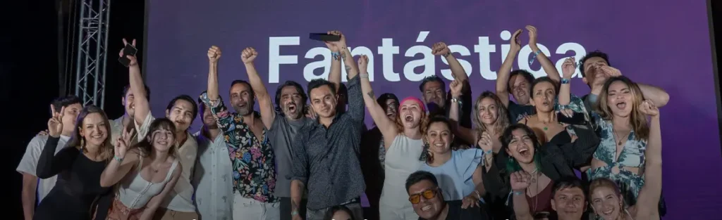 Un grupo de personas se encuentra frente a un fondo morado con la palabra "Fantástica" escrita en él, celebrando su victoria como Effective Agency of the Year, muchos levantan las manos y aplauden.